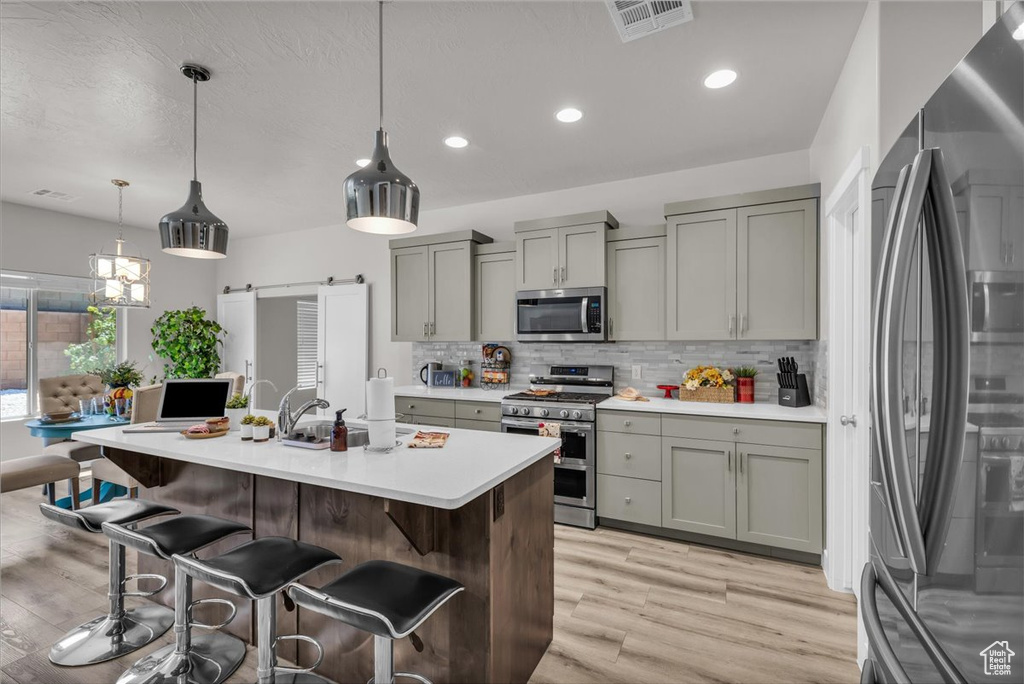 Kitchen featuring appliances with stainless steel finishes, gray cabinets, light wood-type flooring, light countertops, and decorative backsplash
