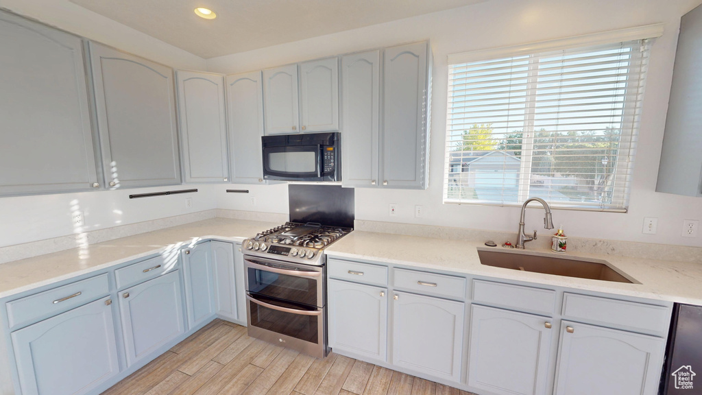 Kitchen with black microwave, double oven range, dishwasher, light wood-type flooring, and light countertops