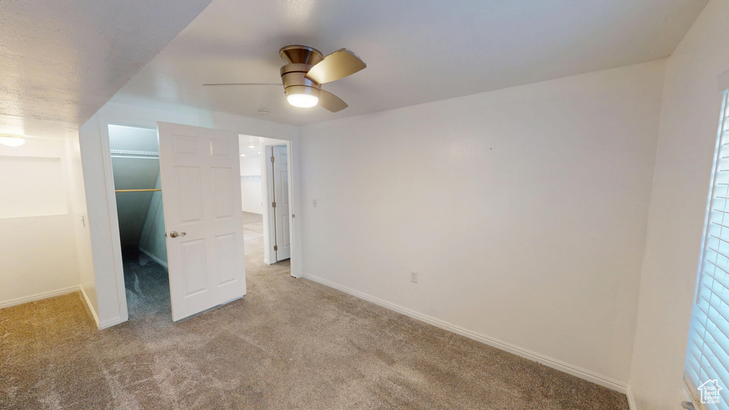 Unfurnished bedroom with carpet, a spacious closet, a ceiling fan, and a closet