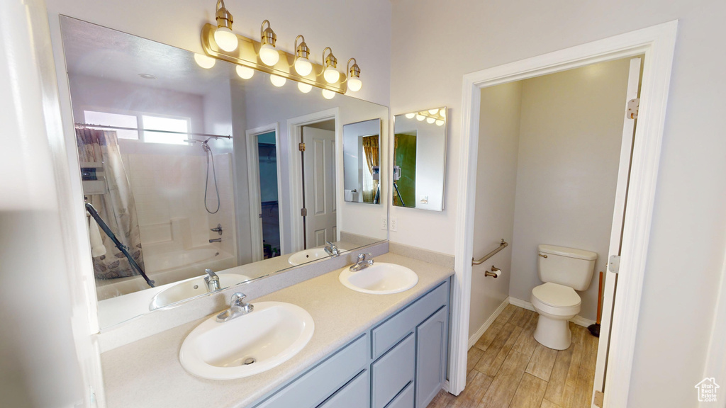 Bathroom with double vanity, shower / tub combo, and wood finished floors