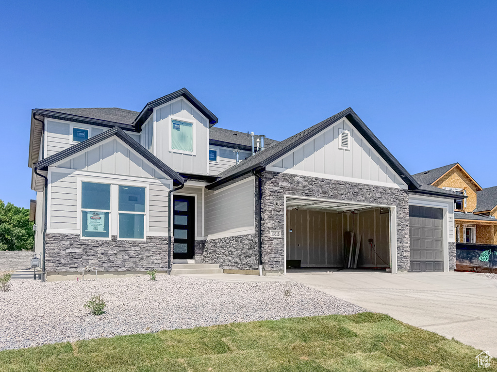 View of front of home featuring a garage, stone siding, concrete driveway, and board and batten siding