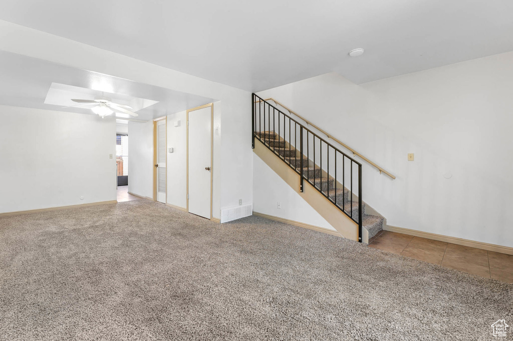 Unfurnished living room featuring stairs, carpet flooring, and a ceiling fan