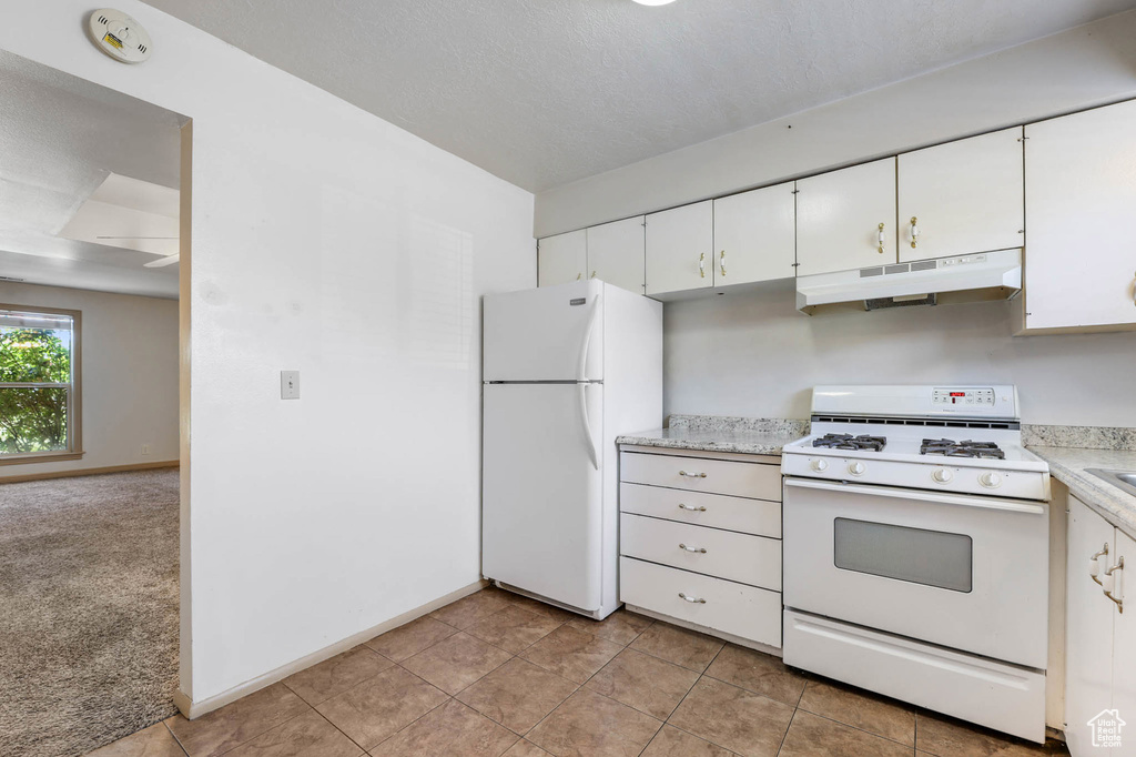 Kitchen featuring white appliances, under cabinet range hood, light countertops, and white cabinetry