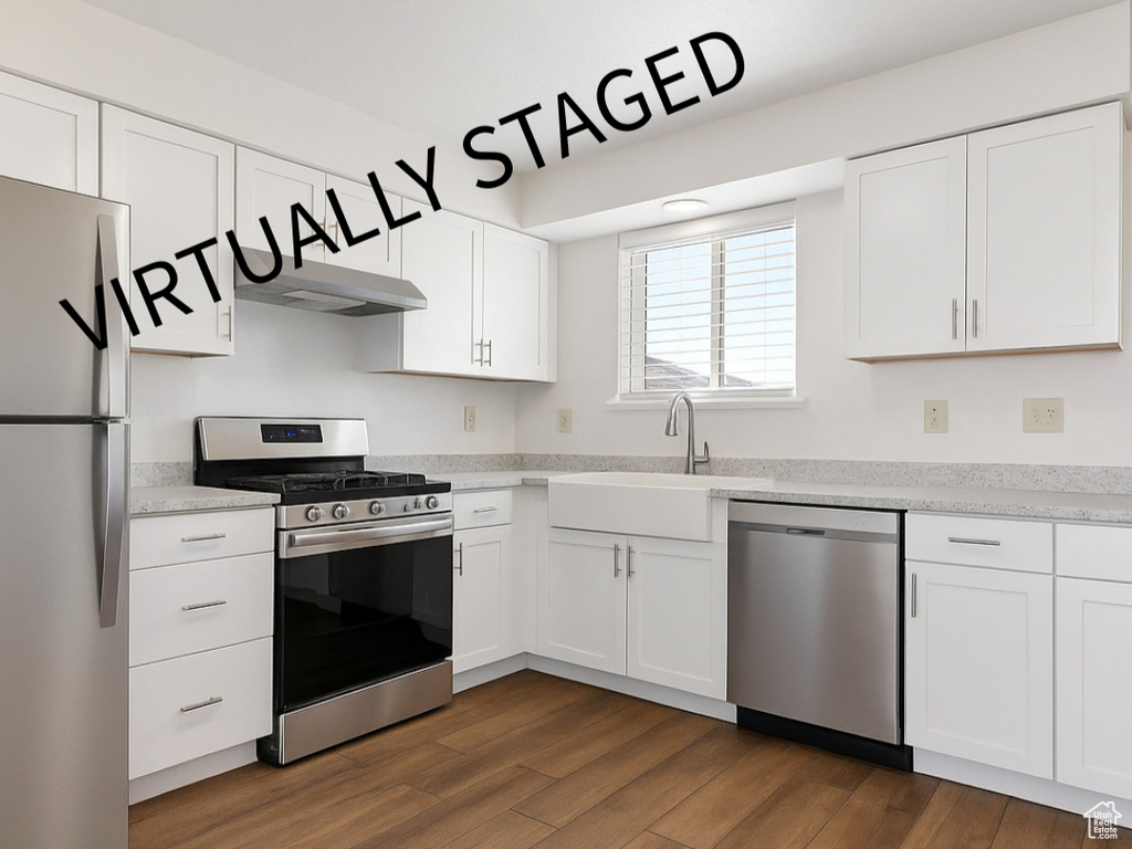 Kitchen featuring stainless steel appliances, under cabinet range hood, dark wood-type flooring, and white cabinetry