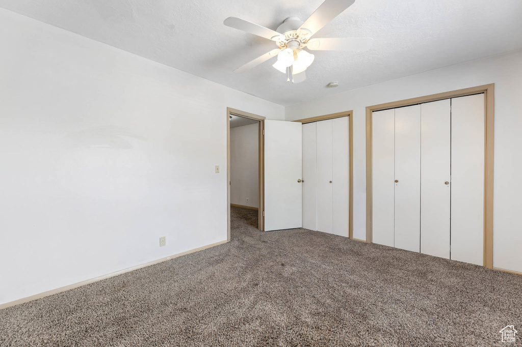 Unfurnished bedroom with carpet, multiple closets, and a ceiling fan