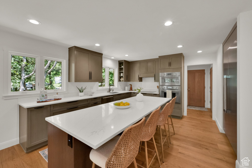 Kitchen with stainless steel appliances, open shelves, light wood-style flooring, a breakfast bar, and recessed lighting