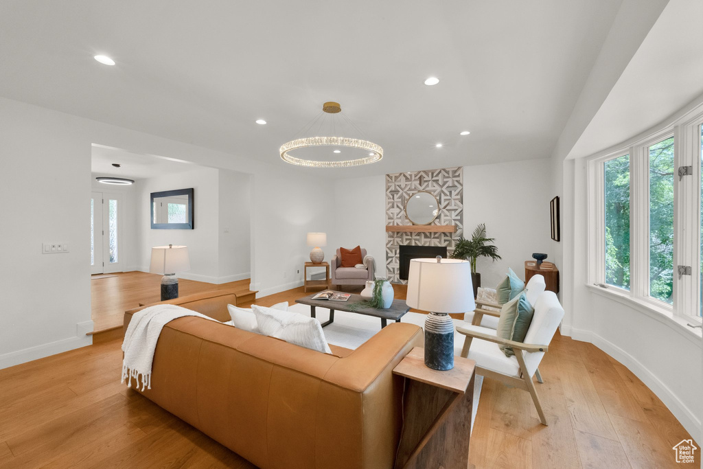 Living area featuring light wood-type flooring, recessed lighting, a chandelier, and a stone fireplace