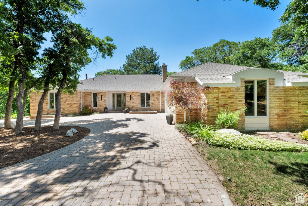Ranch-style house featuring decorative driveway, brick siding, and roof with shingles