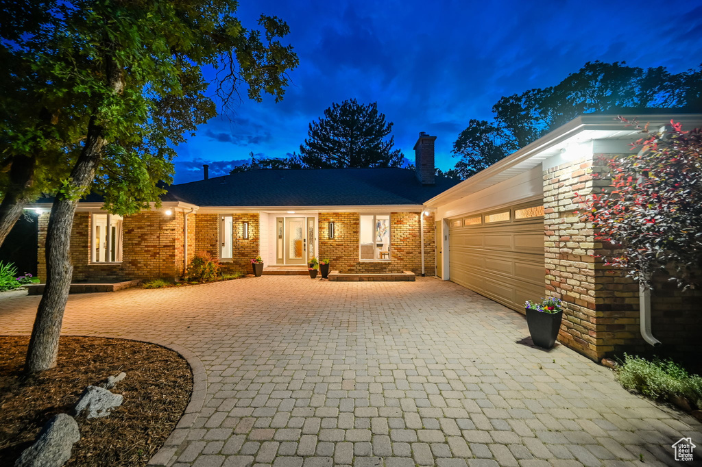 Ranch-style house featuring decorative driveway, a garage, a chimney, and brick siding