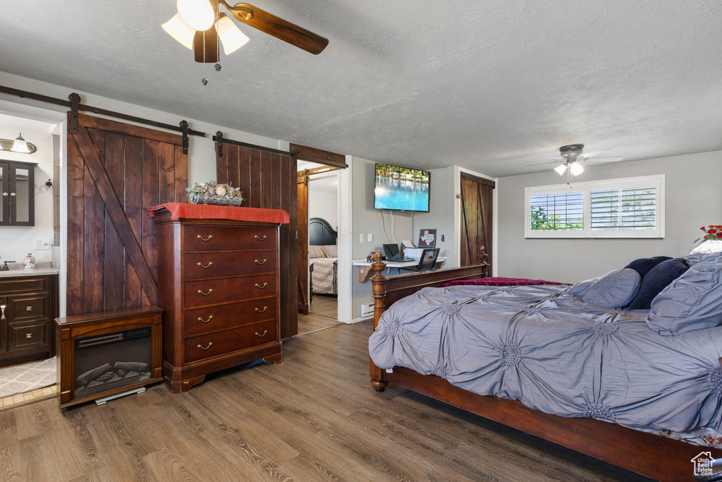 Bedroom featuring light wood-style flooring, a barn door, a textured ceiling, ensuite bathroom, and a ceiling fan