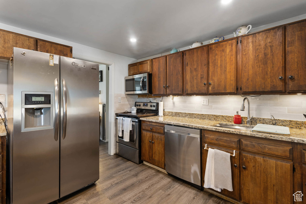 Kitchen with stainless steel appliances, tasteful backsplash, wood finished floors, and light stone countertops