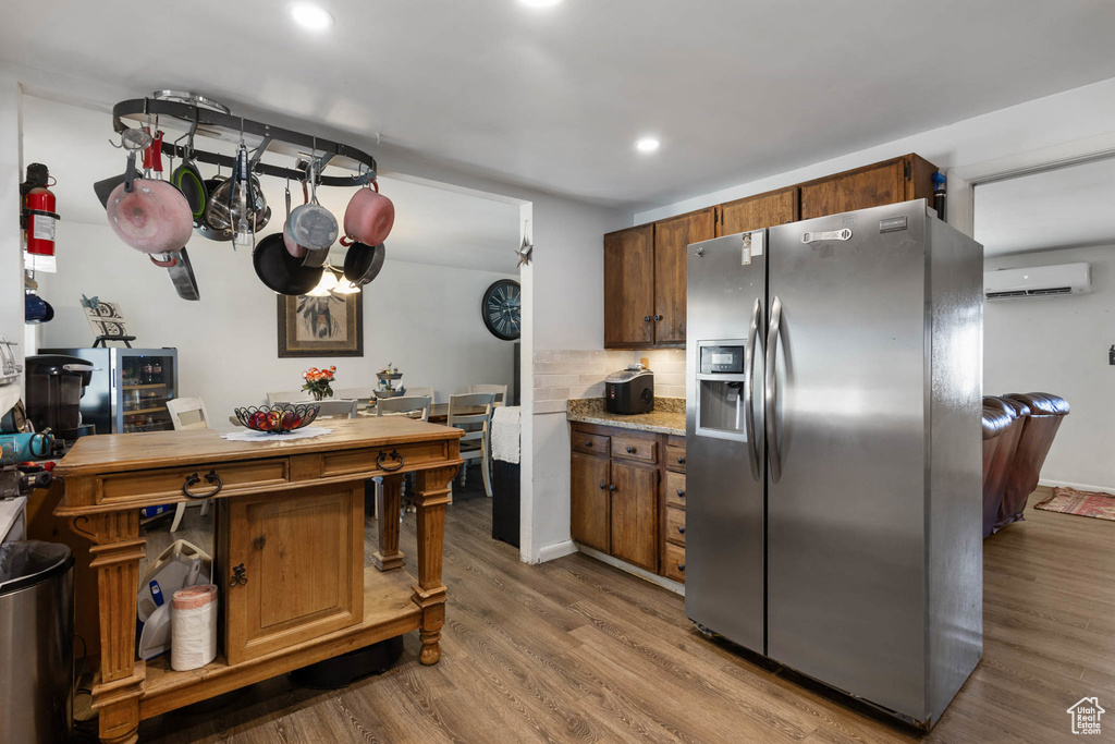 Kitchen with stainless steel fridge, a wall unit AC, wood finished floors, decorative backsplash, and recessed lighting