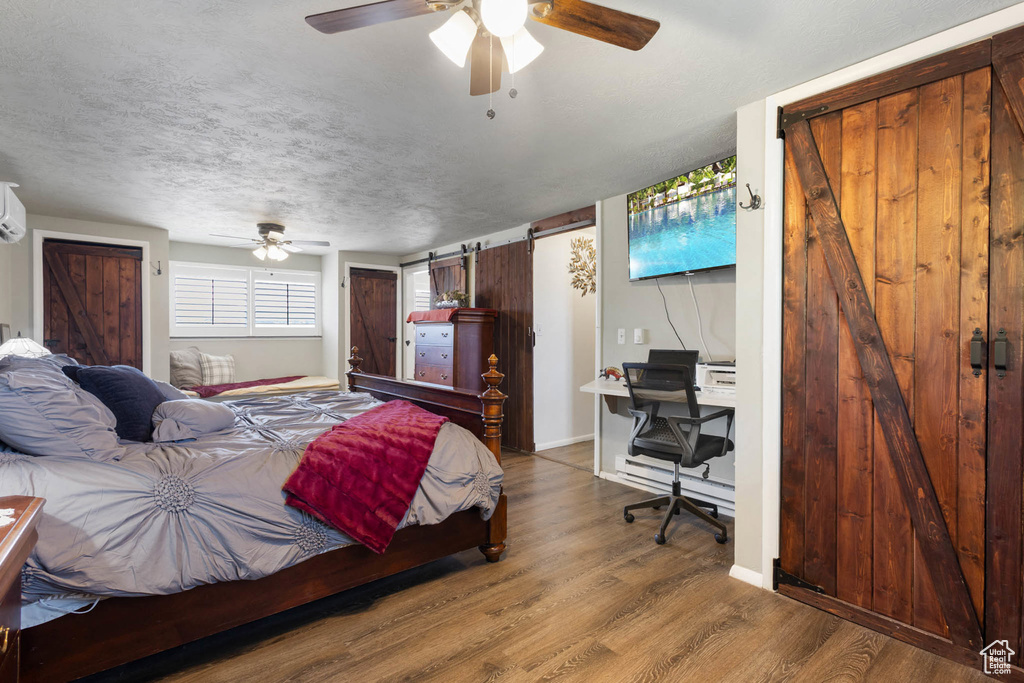 Bedroom featuring a barn door, wood finished floors, a desk, a ceiling fan, and a wall mounted AC