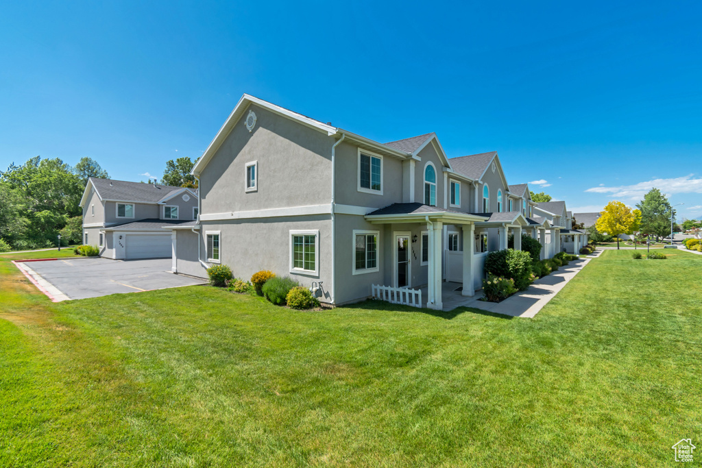 Rear view of house with a garage, a lawn, stucco siding, and a residential view