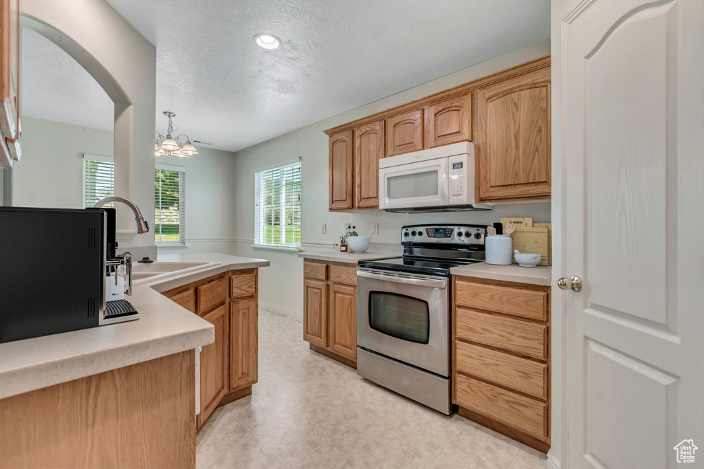 Kitchen featuring white microwave, stainless steel range with electric cooktop, a chandelier, light countertops, and a textured ceiling