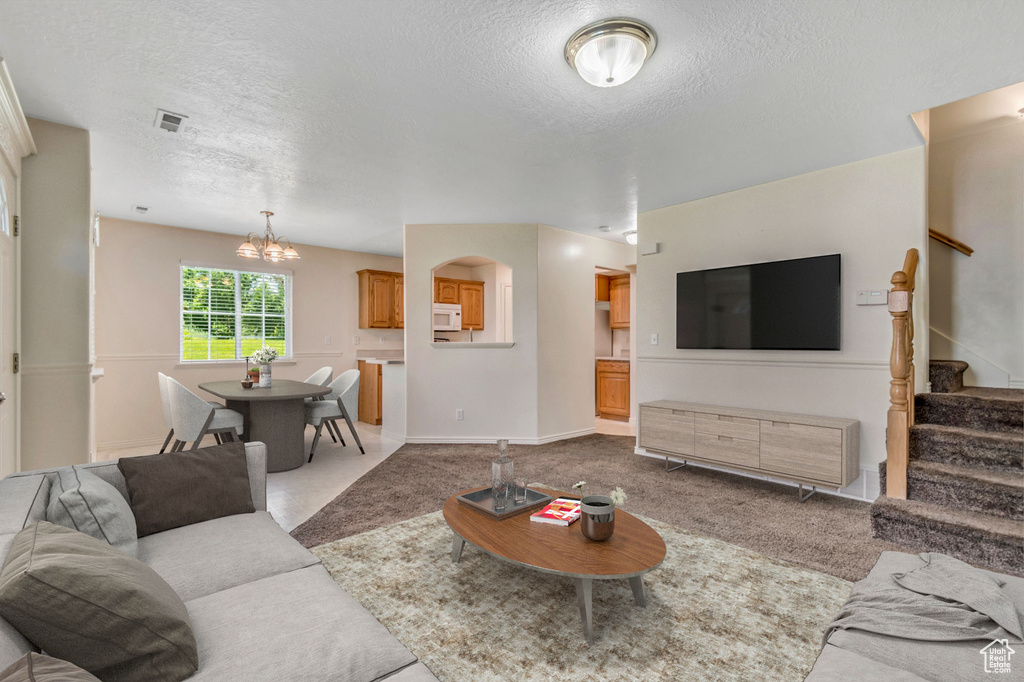 Carpeted living area featuring a textured ceiling, stairway, and a chandelier