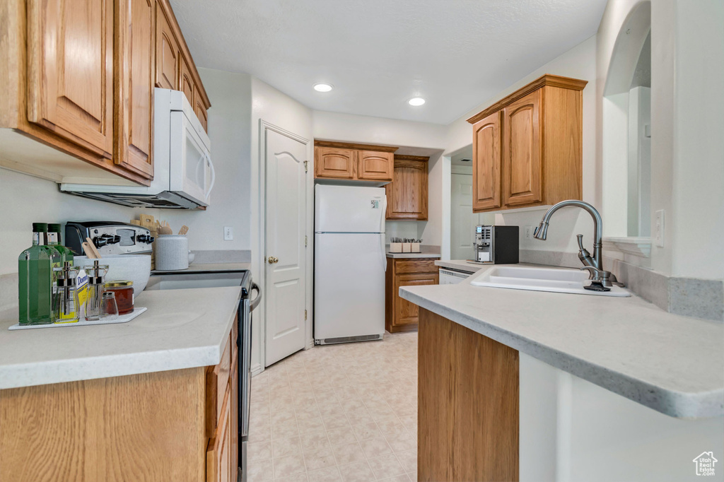 Kitchen featuring white appliances, recessed lighting, light countertops, brown cabinetry, and light flooring