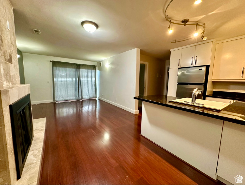 Kitchen featuring freestanding refrigerator, wood finished floors, white cabinets, a tiled fireplace, and dark countertops