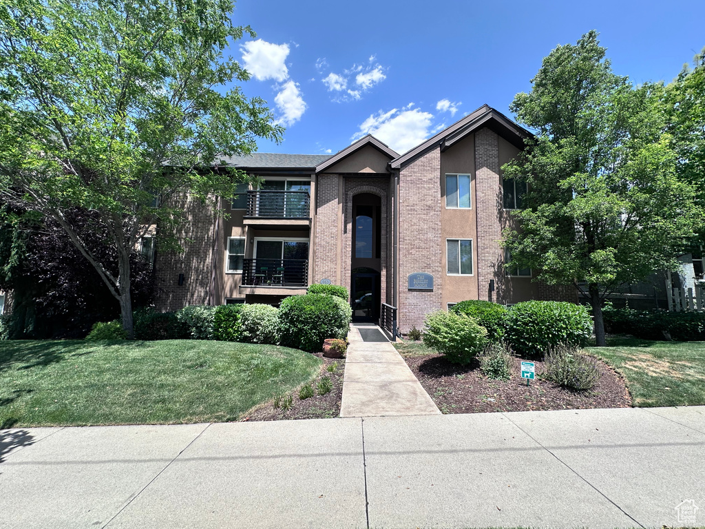 Townhome / multi-family property featuring a front lawn, a balcony, and stucco siding