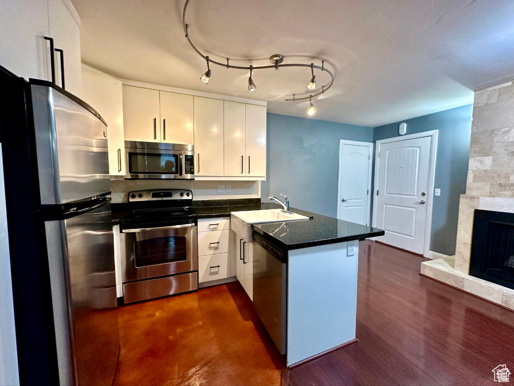 Kitchen featuring stainless steel appliances, a peninsula, white cabinetry, and dark countertops