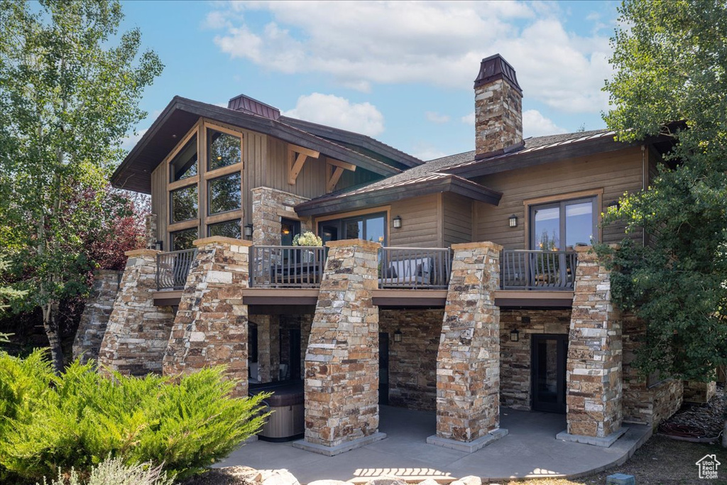Back of property featuring a balcony, stone siding, and a chimney