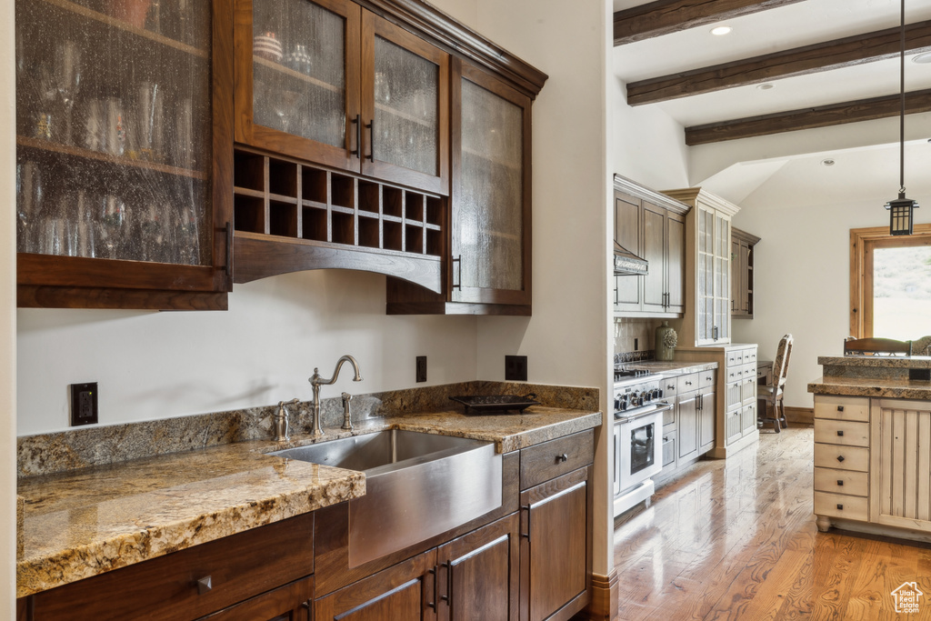 Kitchen featuring beam ceiling, light wood-style floors, high end range, glass insert cabinets, and decorative light fixtures