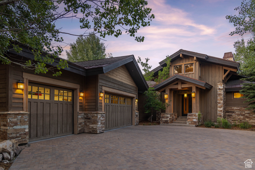 Craftsman-style home featuring stone siding, decorative driveway, a garage, a chimney, and board and batten siding