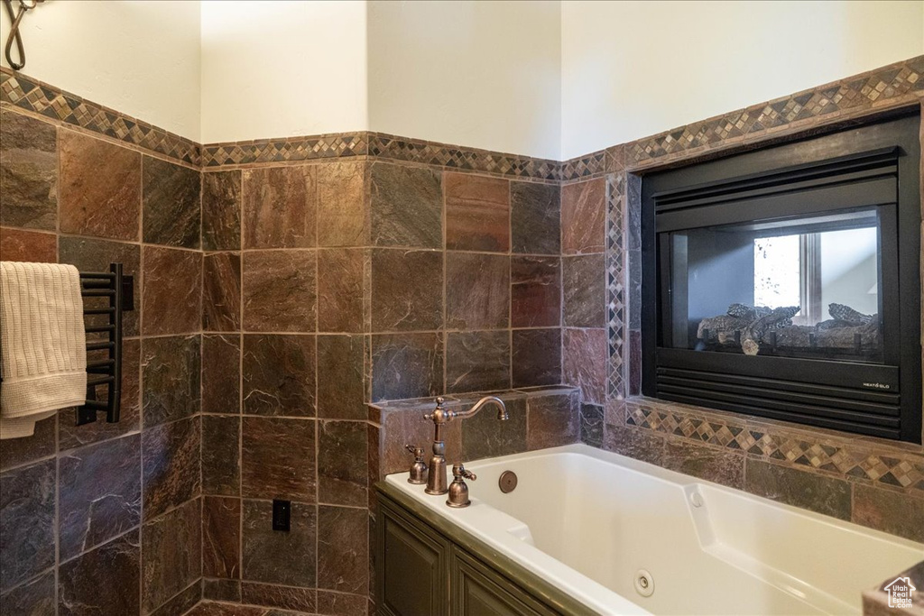 Full bathroom with a jetted tub, tile walls, and a towel warming rack