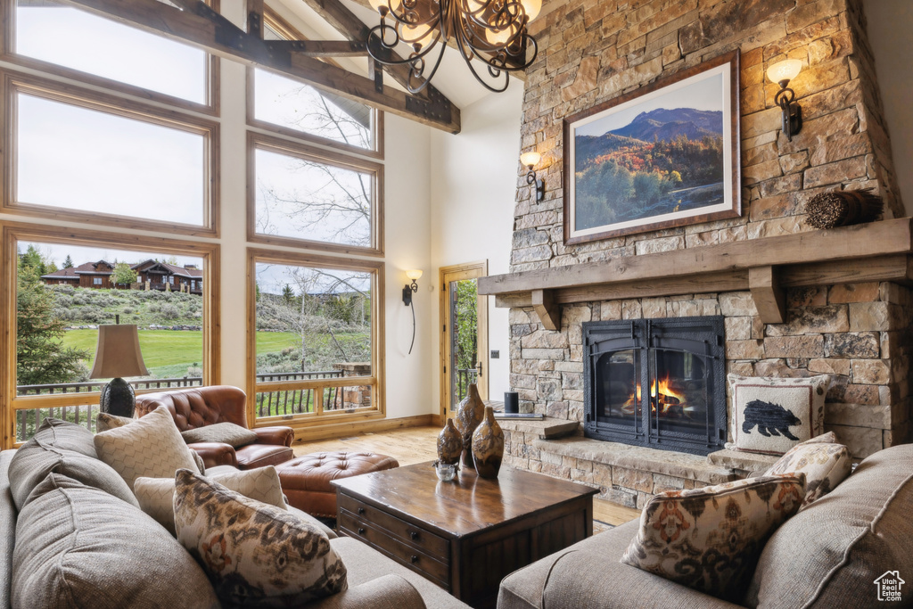 Living room featuring high vaulted ceiling, a chandelier, wood finished floors, and a stone fireplace