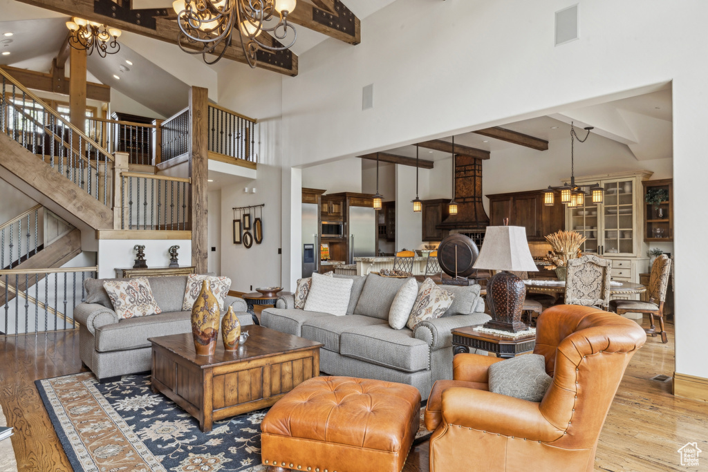 Living room with a chandelier, beamed ceiling, wood finished floors, stairway, and high vaulted ceiling