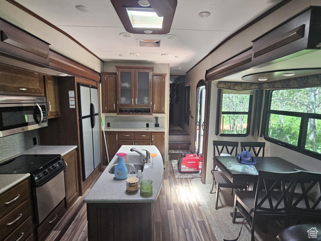 Kitchen with stainless steel appliances, glass insert cabinets, a center island with sink, dark wood-type flooring, and dark brown cabinetry