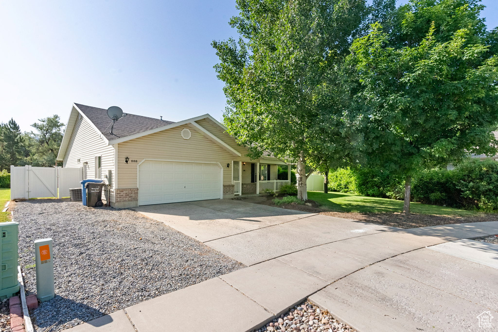 View of front of property featuring an attached garage, driveway, a gate, brick siding, and covered porch