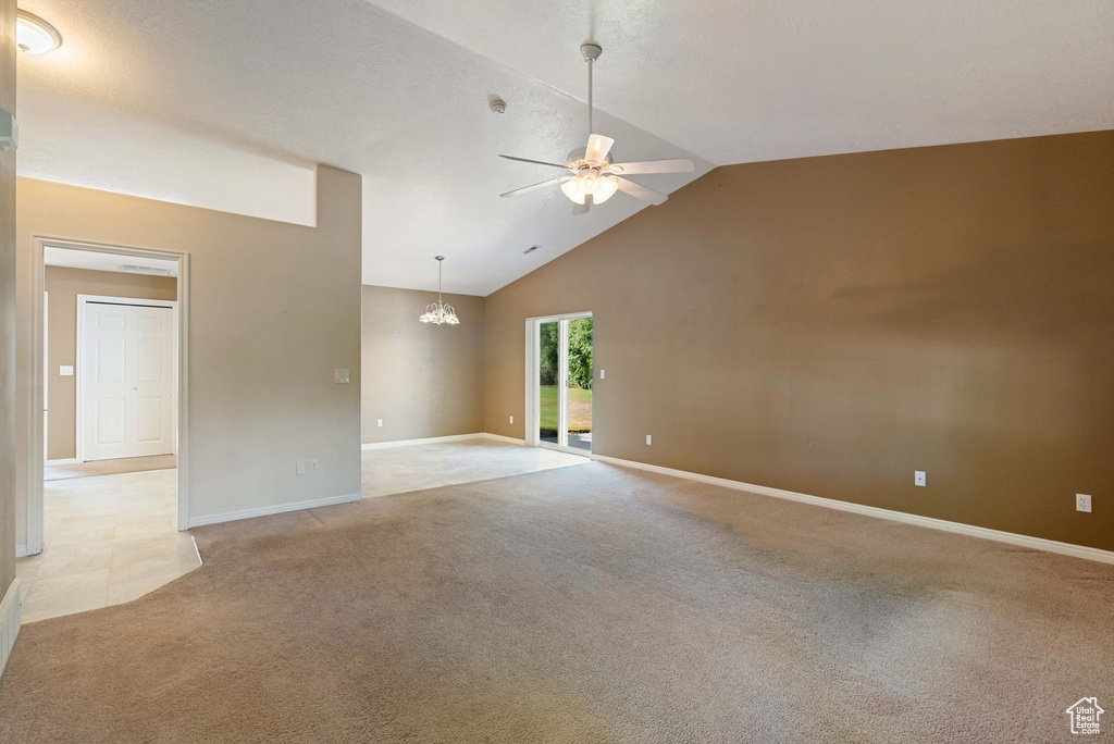 Unfurnished room featuring ceiling fan, light colored carpet, vaulted ceiling, and a chandelier
