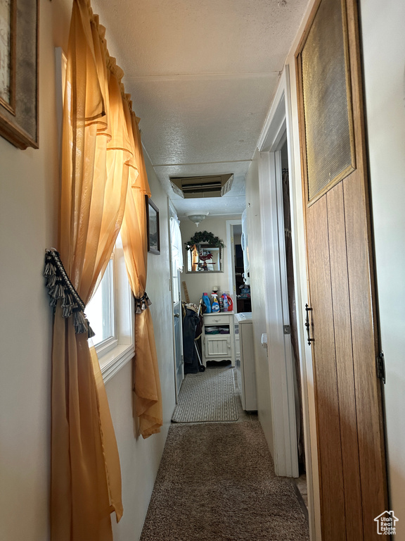 Hallway with light colored carpet and a textured ceiling