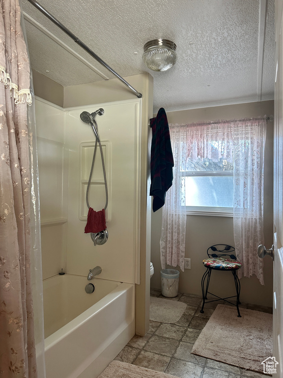 Full bath with stone tile flooring, shower / tub combo, and a textured ceiling