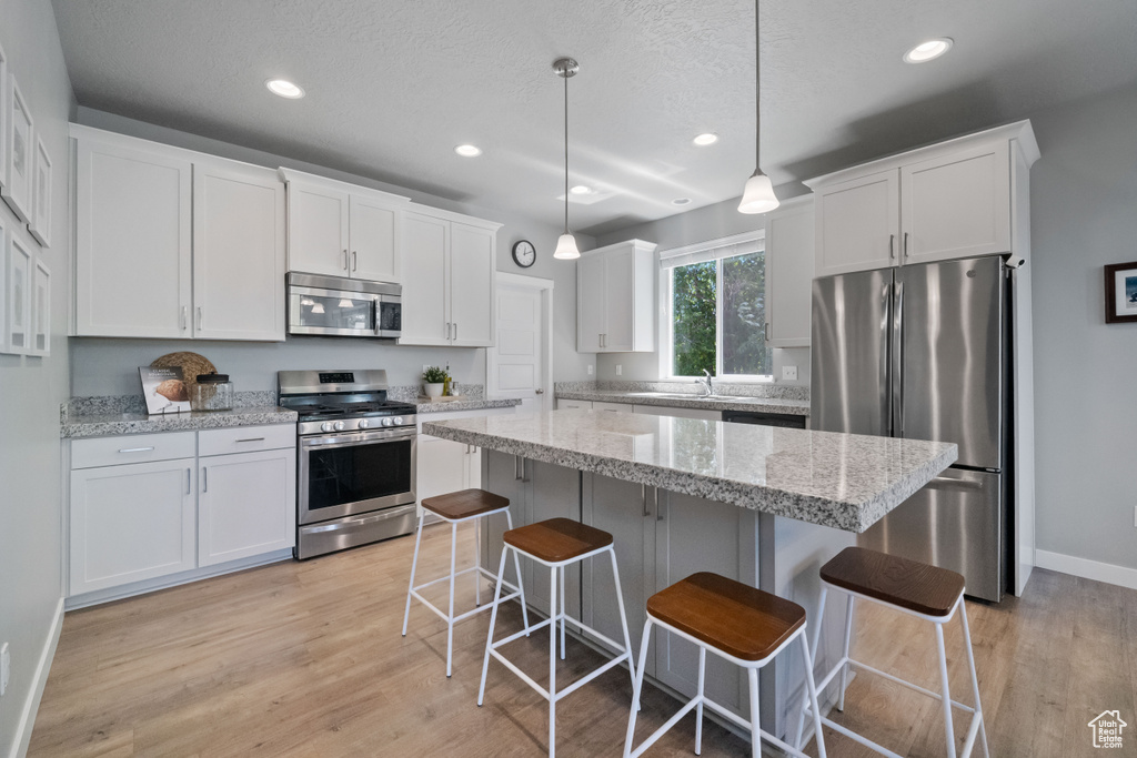 Kitchen featuring stainless steel appliances, recessed lighting, white cabinetry, light wood finished floors, and a center island