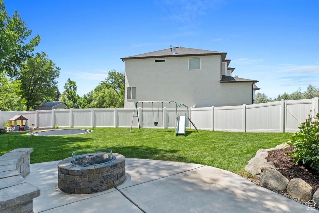 Fenced backyard with a playground, a patio area, and a fire pit