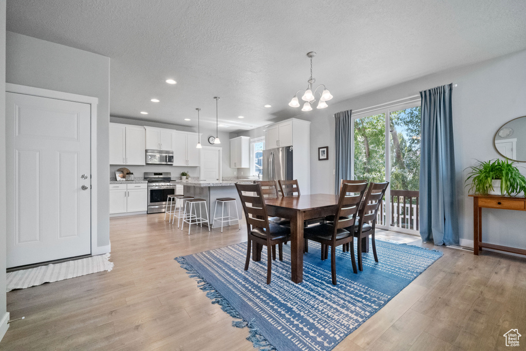 Dining area with light wood finished floors, a chandelier, recessed lighting, and a textured ceiling