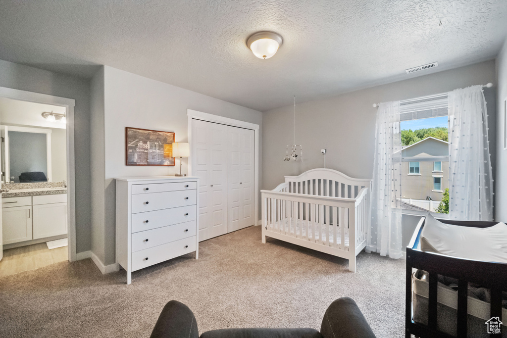 Bedroom featuring light colored carpet, a closet, a textured ceiling, and connected bathroom