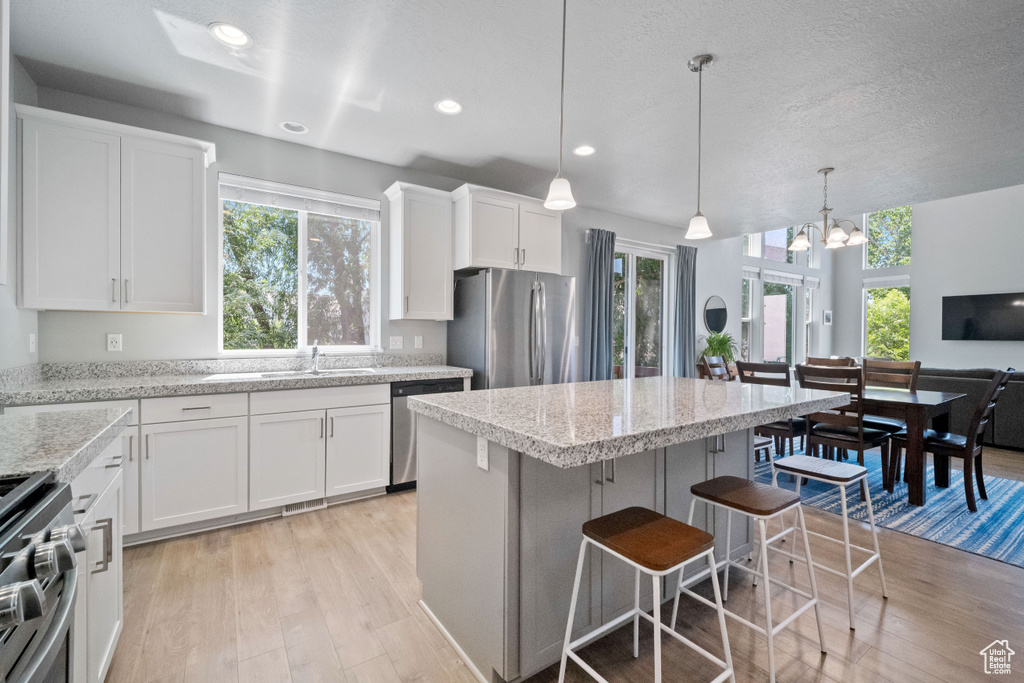 Kitchen with appliances with stainless steel finishes, light wood-type flooring, a breakfast bar, white cabinetry, and a kitchen island