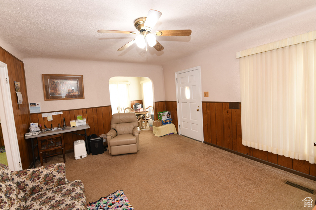 Carpeted living area featuring wainscoting, wood walls, arched walkways, and ceiling fan