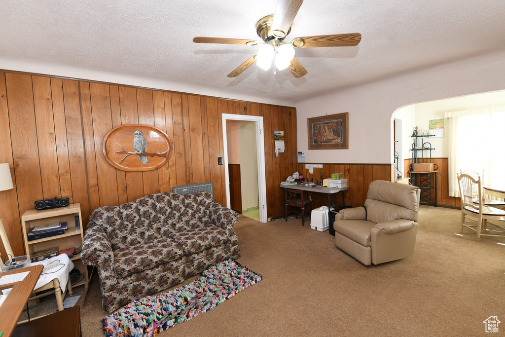 Carpeted living room featuring wood walls, a ceiling fan, arched walkways, and a wainscoted wall