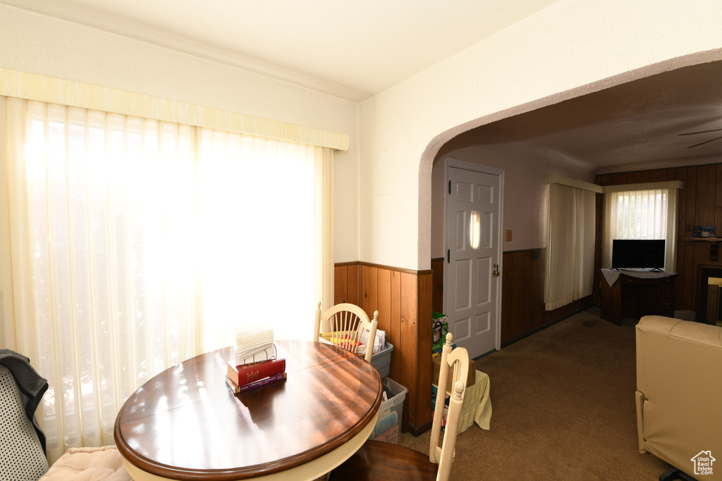 Carpeted dining room with arched walkways, wood walls, and a wainscoted wall
