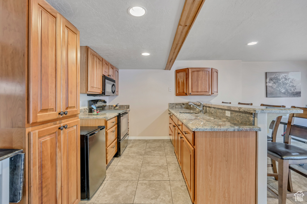 Kitchen with black appliances, a kitchen bar, a peninsula, light stone counters, and recessed lighting