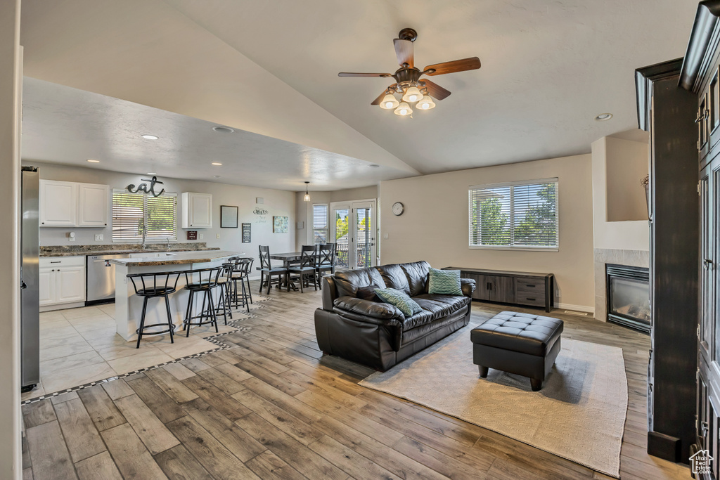 Living room with a ceiling fan, a tile fireplace, plenty of natural light, lofted ceiling, and light wood-style floors