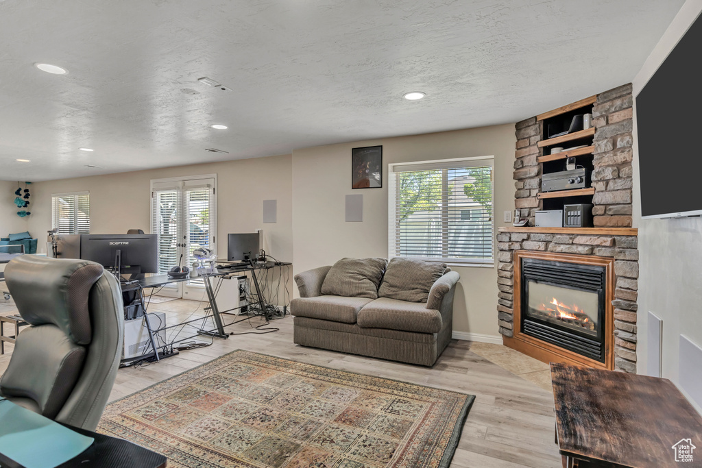 Living area with plenty of natural light, a stone fireplace, an office area, wood finished floors, and recessed lighting