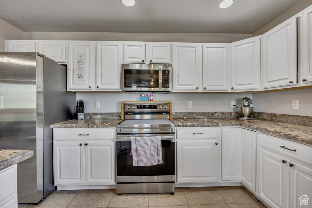 Kitchen featuring appliances with stainless steel finishes, white cabinetry, and stone counters