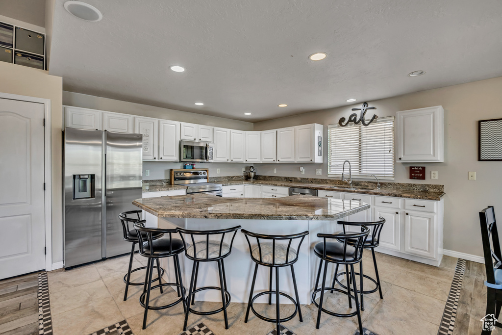 Kitchen featuring appliances with stainless steel finishes, a kitchen breakfast bar, a kitchen island, white cabinets, and recessed lighting