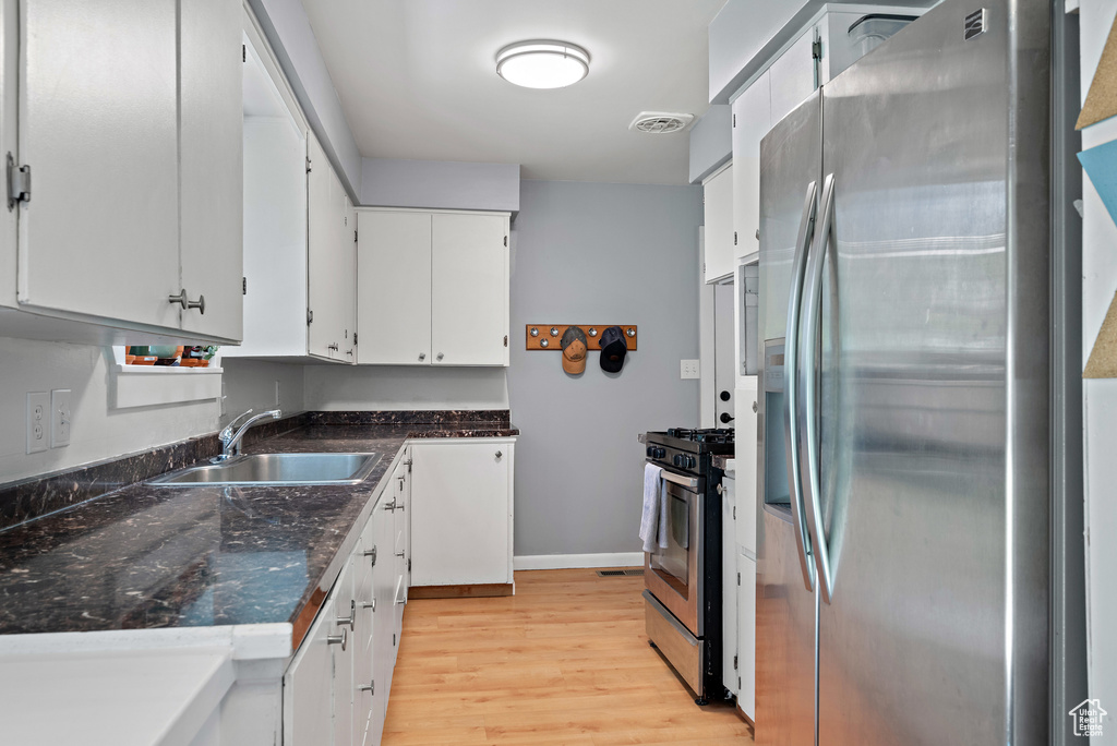 Kitchen with appliances with stainless steel finishes, light wood-style flooring, white cabinetry, and dark stone counters