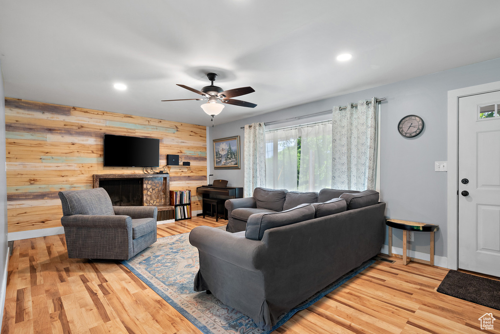 Living area featuring wood walls, a ceiling fan, recessed lighting, light wood finished floors, and a fireplace with raised hearth
